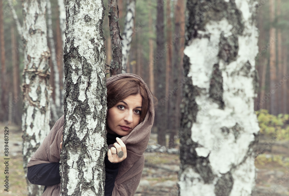 A girl in a long dress with a brown scarf on her head in a dark autumn birch forest. A girl in a long dress with a brown scarf on her head in a dark autumn birch forest.
