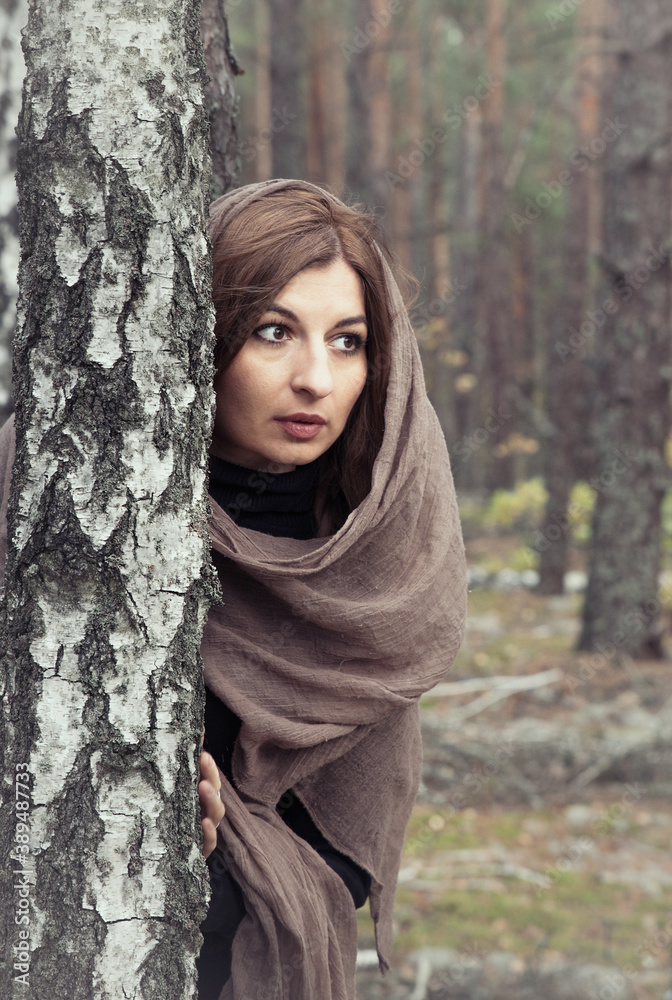 A girl in a long dress with a brown scarf on her head in a dark autumn birch forest. A girl in a long dress with a brown scarf on her head in a dark autumn birch forest.