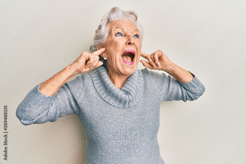 Senior grey-haired woman covering ears with finger angry and mad screaming frustrated and furious, shouting with anger. rage and aggressive concept. Senior grey-haired woman covering ears with finger angry and mad screaming frustrated and furious, shouting with anger. rage and aggressive concept.