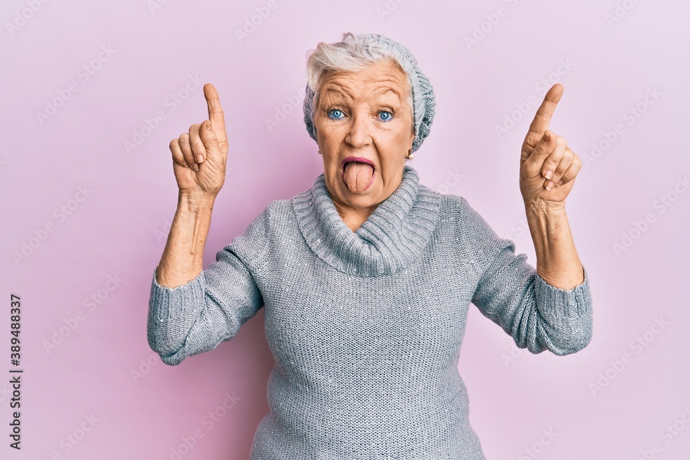 Senior grey-haired woman pointing up with fingers sticking tongue out happy with funny expression. Senior grey-haired woman pointing up with fingers sticking tongue out happy with funny expression.