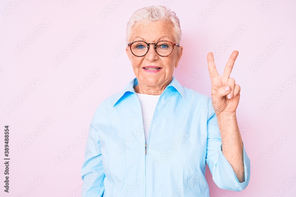 Senior beautiful woman with blue eyes and grey hair wearing glasses smiling with happy face winking at the camera doing victory sign. number two. Senior beautiful woman with blue eyes and grey hair wearing glasses smiling with happy face winking at the camera doing victory sign. number two.