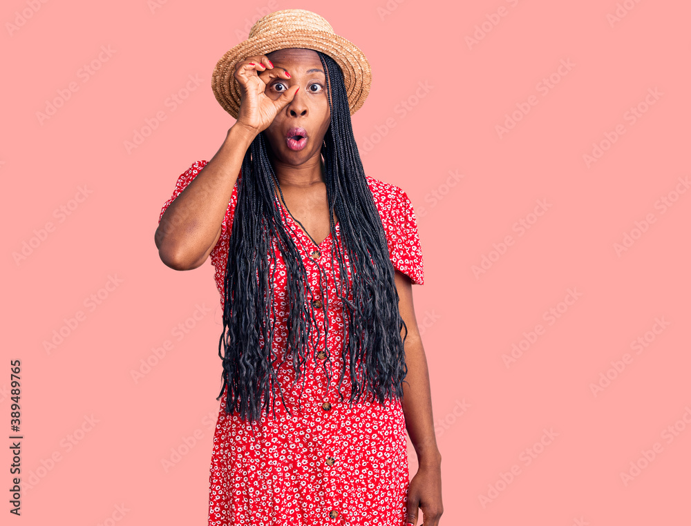 Young african american woman wearing summer hat doing ok gesture shocked with surprised face, eye looking through fingers. unbelieving expression. Young african american woman wearing summer hat doing ok gesture shocked with surprised face, eye looking through fingers. unbelieving expression.