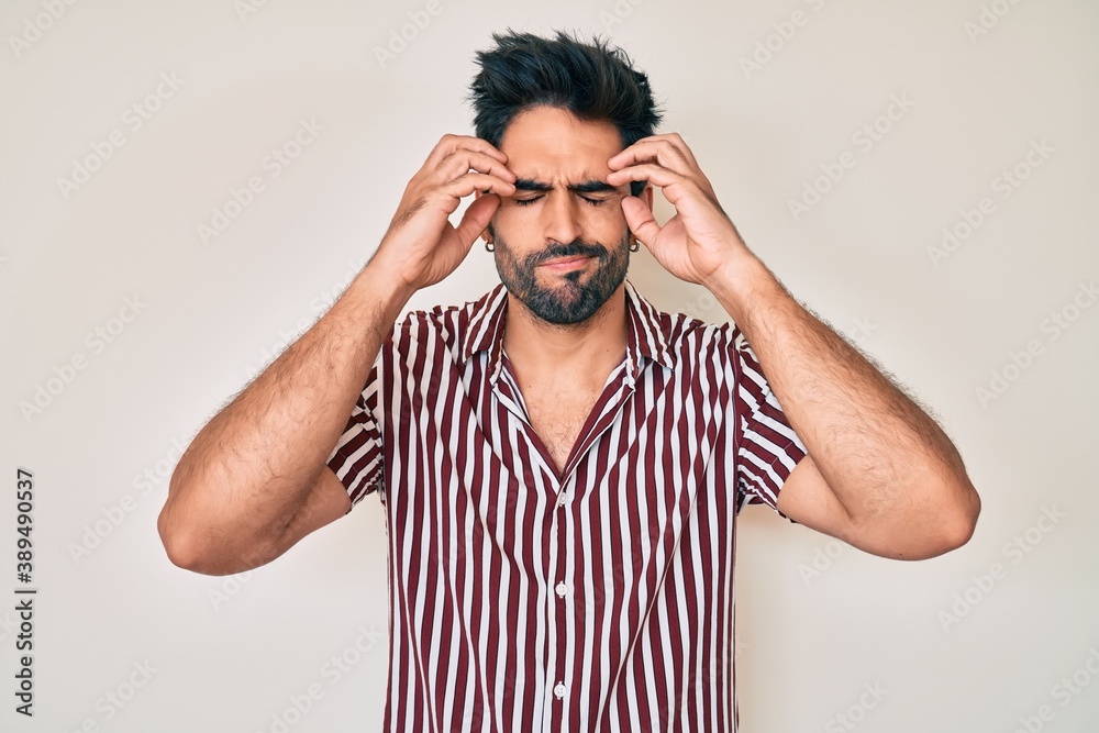 Handsome hispanic man with beard wearing casual clothes suffering from headache desperate and stressed because pain and migraine. hands on head. Handsome hispanic man with beard wearing casual clothes suffering from headache desperate and stressed because pain and migraine. hands on head.