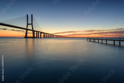 Background with colourful sunrise on the Lisbon bridge. The Vasco da Gama Bridge is a landmark, and one of the longest bridges in the world.  Portugal is an amazing tourist destination. © aroxopt
