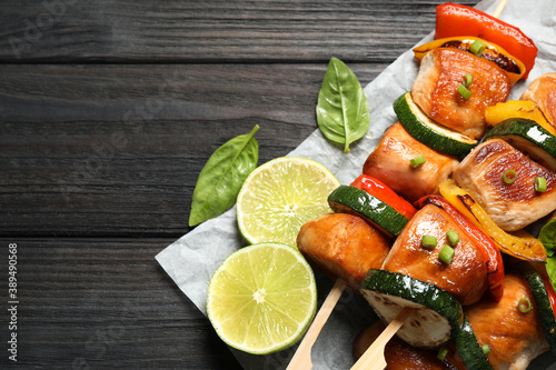 Delicious chicken shish kebabs with vegetables and lime on black wooden table, top view. Space for text