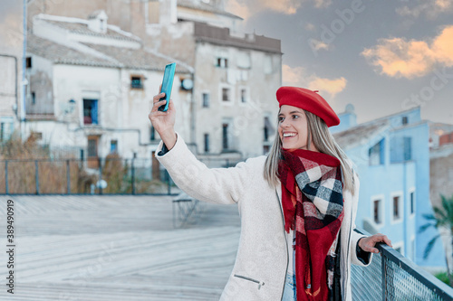 Young smiling woman taking a picture with her mobile phone during the sunset.