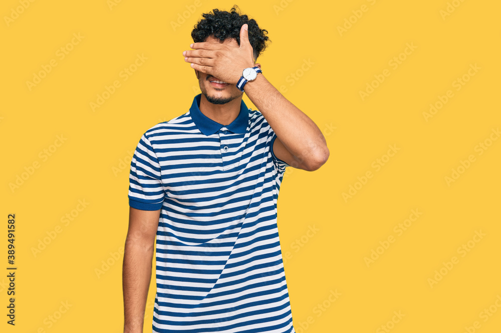 Young arab man wearing casual clothes and glasses smiling and laughing with hand on face covering eyes for surprise. blind concept. Young arab man wearing casual clothes and glasses smiling and laughing with hand on face covering eyes for surprise. blind concept.