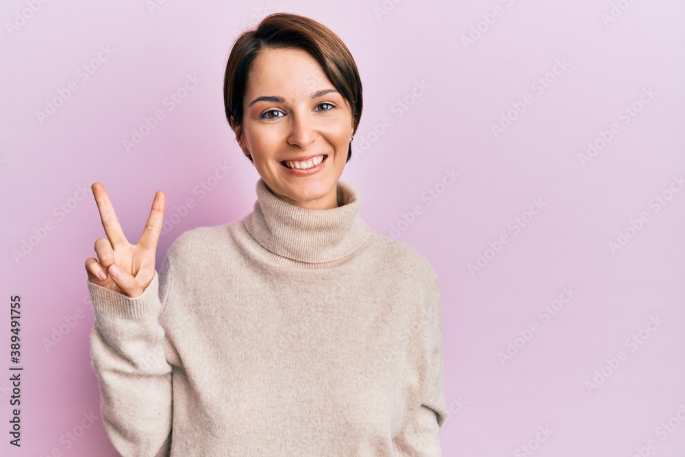 Young brunette woman with short hair wearing casual winter sweater showing and pointing up with fingers number two while smiling confident and happy. Young brunette woman with short hair wearing casual winter sweater showing and pointing up with fingers number two while smiling confident and happy.