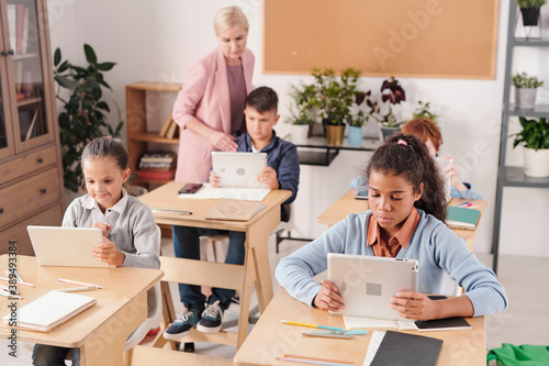 Group of contemporary schoolchildren with tablets working by desks in two rows