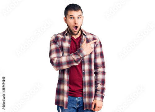 Young handsome man wearing casual shirt surprised pointing with finger to the side, open mouth amazed expression.
