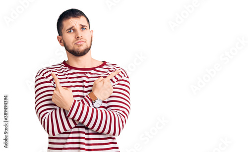Young handsome man wearing striped sweater pointing to both sides with fingers, different direction disagree