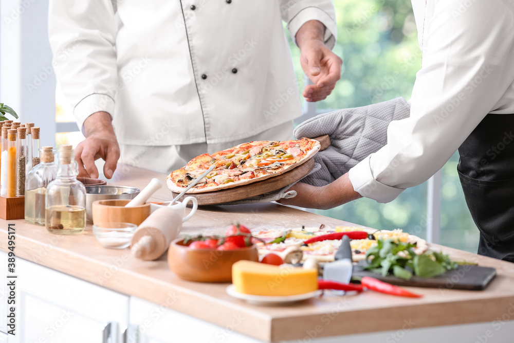 Mature chefs with tasty pizza in kitchen Mature chefs with tasty pizza in kitchen