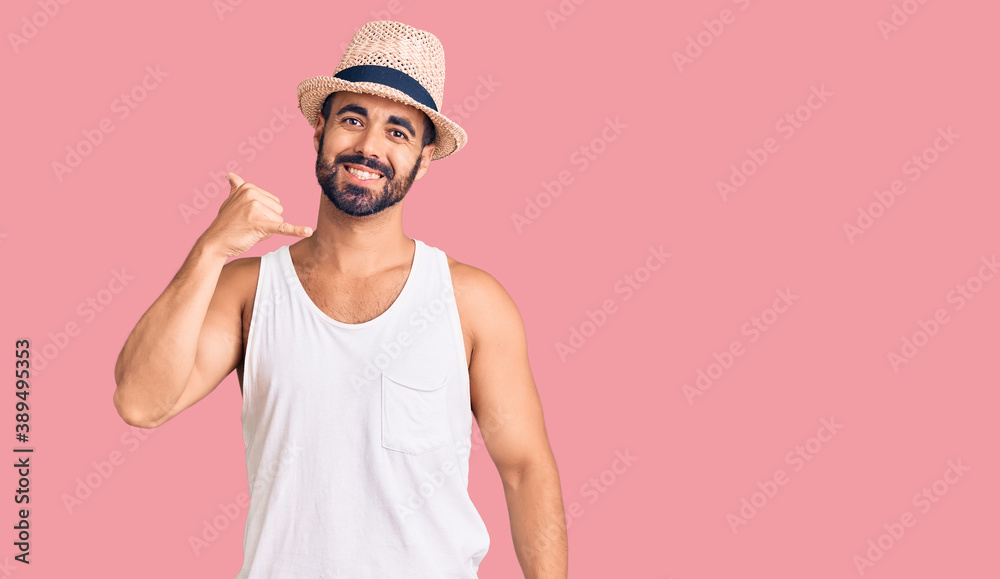 Young hispanic man wearing casual summer hat smiling doing phone gesture with hand and fingers like talking on the telephone. communicating concepts. Young hispanic man wearing casual summer hat smiling doing phone gesture with hand and fingers like talking on the telephone. communicating concepts.