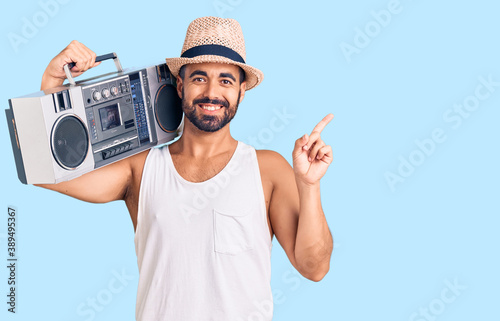 Young hispanic man holding boombox, listening to music smiling happy pointing with hand and finger to the side