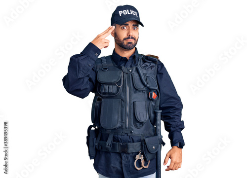 Young hispanic man wearing police uniform shooting and killing oneself pointing hand and fingers to head like gun, suicide gesture.