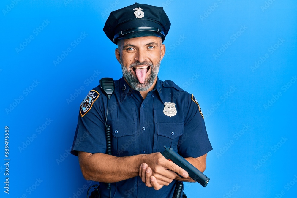 Middle age handsome man wearing police uniform holding gun sticking tongue out happy with funny expression. Middle age handsome man wearing police uniform holding gun sticking tongue out happy with funny expression.
