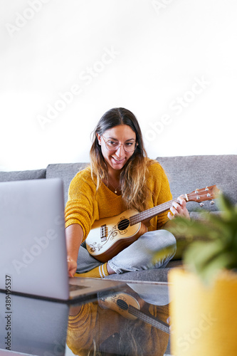 Woman learning to play ukulele online from her laptop during covid quarantine. photo