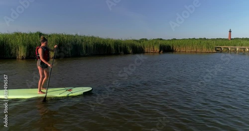 Attractive female on a stand up paddleboard in the Currituck sound in the Outer Banks with a lighthouse in the background