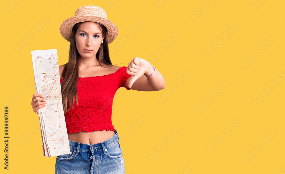 Young beautiful hispanic woman wearing summer hat holding city map with angry face, negative sign showing dislike with thumbs down, rejection concept Young beautiful hispanic woman wearing summer hat holding city map with angry face, negative sign showing dislike with thumbs down, rejection concept