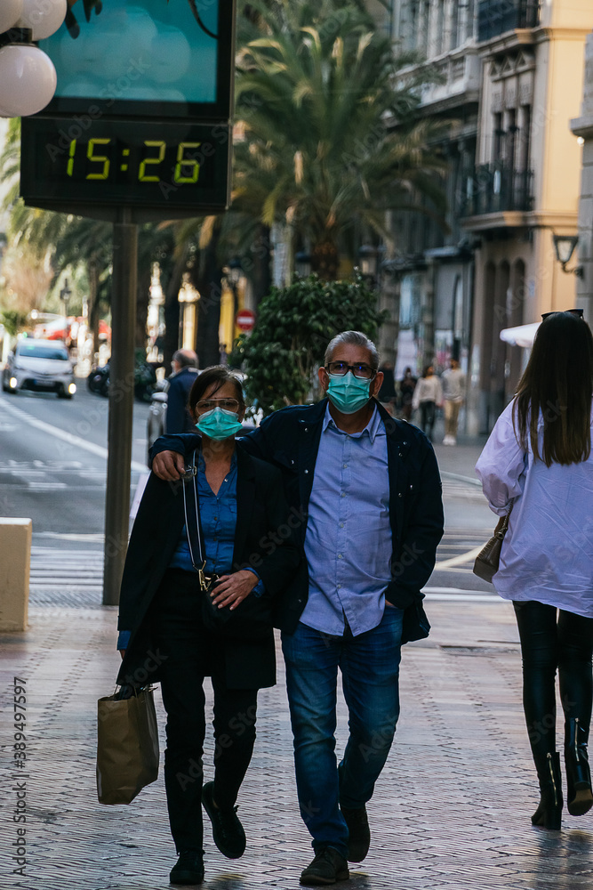 caucasian couple of about 50 years old walking in the city during the covid-19 pandemic. The man hugs the woman with one arm as they walk. Both wear the mandatory mask for safety. caucasian couple of about 50 years old walking in the city during the covid-19 pandemic. The man hugs the woman with one arm as they walk. Both wear the mandatory mask for safety.