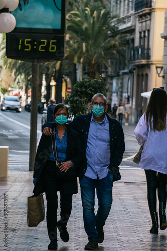 caucasian couple of about 50 years old walking in the city during the covid-19 pandemic. The man hugs the woman with one arm as they walk. Both wear the mandatory mask for safety.