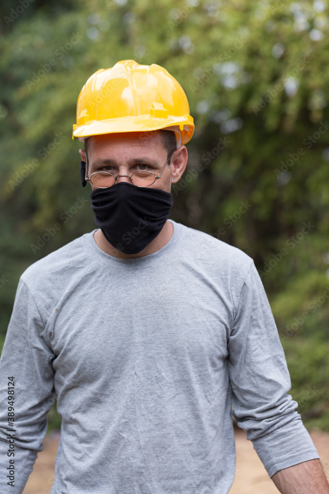 Portrait of a builder or repairman in protective helmet and facial mask. Manual worker portrait wearing safety gear. He wears face mask due to COVID-19. Portrait of a builder or repairman in protective helmet and facial mask. Manual worker portrait wearing safety gear. He wears face mask due to COVID-19.