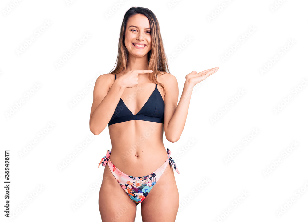 Young beautiful girl wearing bikini amazed and smiling to the camera while presenting with hand and pointing with finger. Young beautiful girl wearing bikini amazed and smiling to the camera while presenting with hand and pointing with finger.