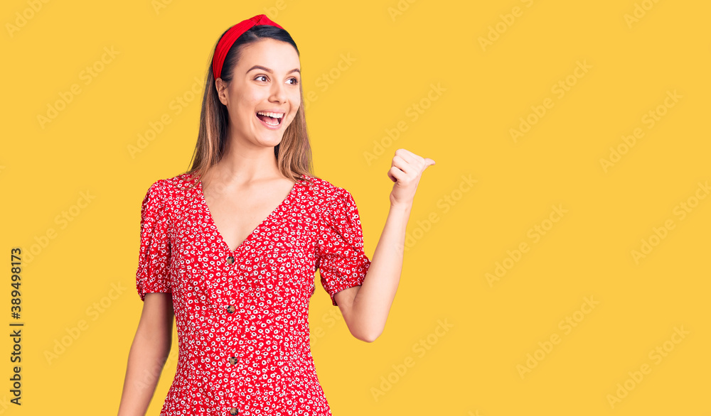 Young beautiful girl wearing dress and diadem smiling with happy face looking and pointing to the side with thumb up. Young beautiful girl wearing dress and diadem smiling with happy face looking and pointing to the side with thumb up.