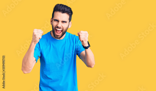 Young handsome man with beard wearing casual t-shirt angry and mad raising fists frustrated and furious while shouting with anger. rage and aggressive concept.