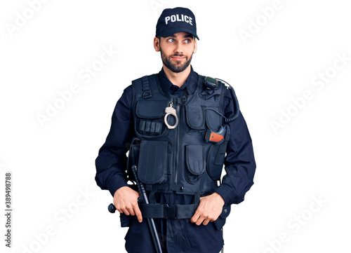 Young handsome man with beard wearing police uniform smiling looking to the side and staring away thinking.