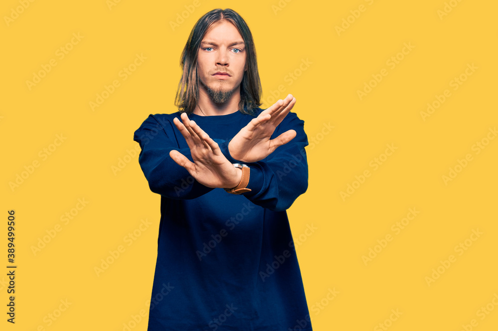 Handsome caucasian man with long hair wearing casual winter sweater rejection expression crossing arms doing negative sign, angry face