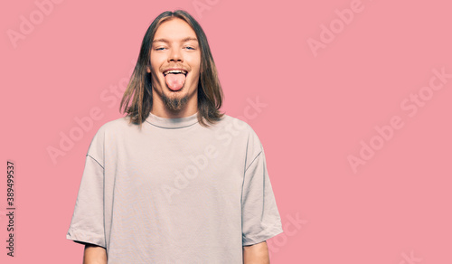 Handsome caucasian man with long hair wearing casual clothes sticking tongue out happy with funny expression. emotion concept.
