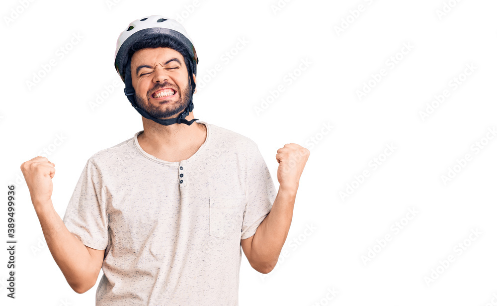 Young hispanic man wearing bike helmet very happy and excited doing winner gesture with arms raised, smiling and screaming for success. celebration concept. Young hispanic man wearing bike helmet very happy and excited doing winner gesture with arms raised, smiling and screaming for success. celebration concept.