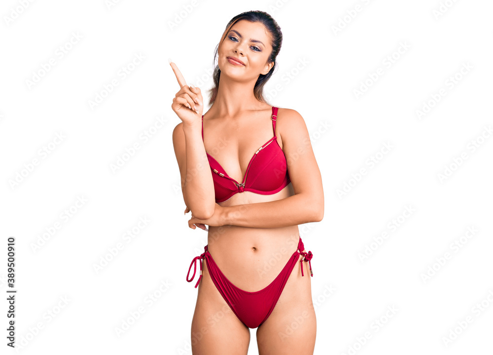 Young beautiful woman wearing bikini pointing finger up with successful idea. exited and happy. number one. Young beautiful woman wearing bikini pointing finger up with successful idea. exited and happy. number one.