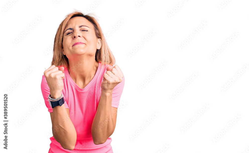 Young blonde woman wearing sportswear excited for success with arms raised and eyes closed celebrating victory smiling. winner concept. Young blonde woman wearing sportswear excited for success with arms raised and eyes closed celebrating victory smiling. winner concept.