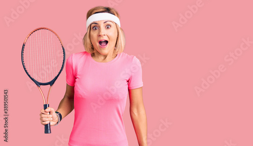 Young blonde woman playing tennis holding racket scared and amazed with open mouth for surprise, disbelief face