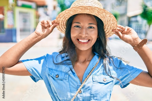 Young beautiful indian woman wearing summer hat smiling happy walking at the city.