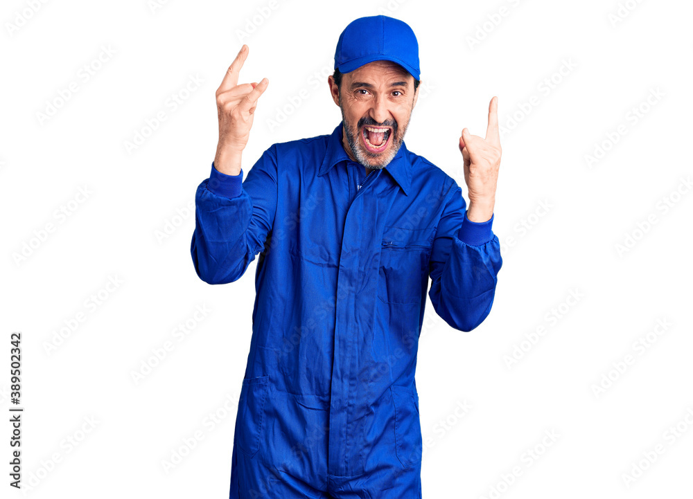 Middle age handsome man wearing mechanic uniform shouting with crazy expression doing rock symbol with hands up. music star. heavy music concept.