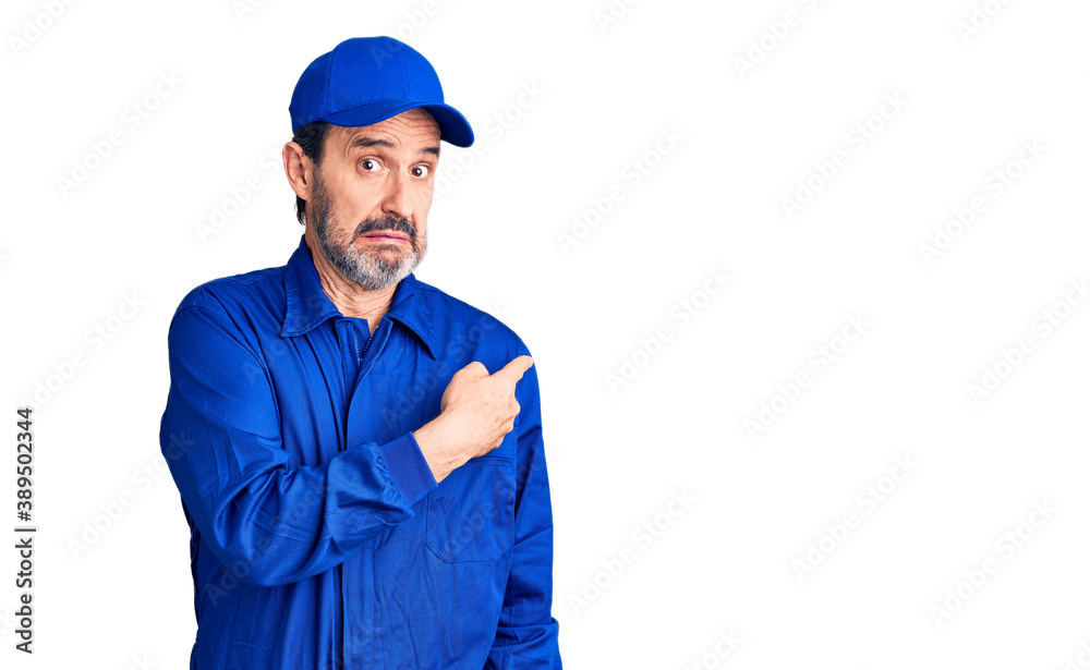 Middle age handsome man wearing mechanic uniform pointing aside worried and nervous with forefinger, concerned and surprised expression