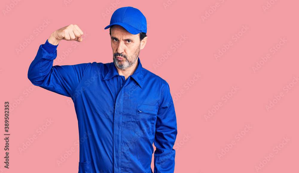 Middle age handsome man wearing mechanic uniform strong person showing arm muscle, confident and proud of power