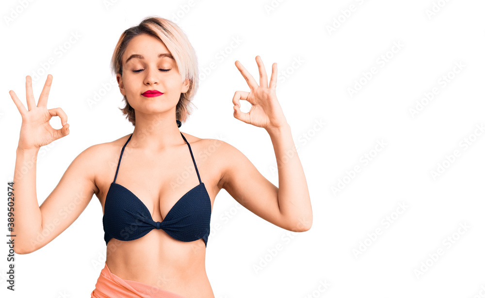 Young beautiful blonde woman wearing bikini relax and smiling with eyes closed doing meditation gesture with fingers. yoga concept. Young beautiful blonde woman wearing bikini relax and smiling with eyes closed doing meditation gesture with fingers. yoga concept.