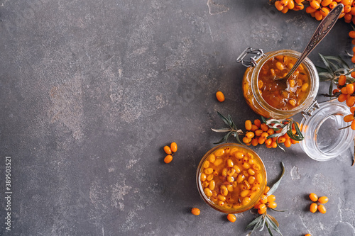 Delicious sea buckthorn jam and fresh berries on grey table, flat lay. Space for text