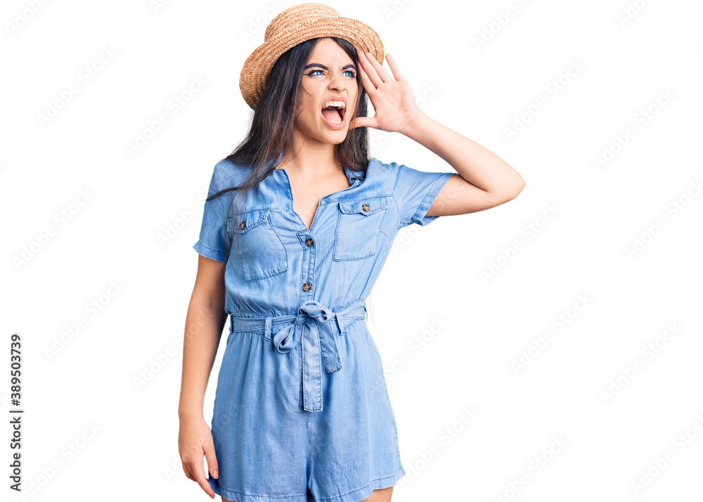 Brunette teenager girl wearing summer hat shouting and screaming loud to side with hand on mouth. communication concept. Brunette teenager girl wearing summer hat shouting and screaming loud to side with hand on mouth. communication concept.