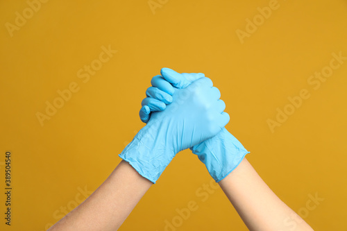 Doctors in medical gloves shaking hands on yellow background, closeup