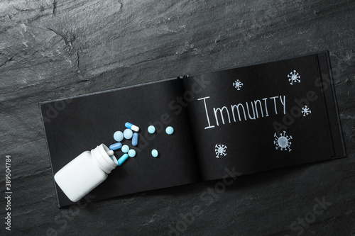 Notebook with word Immunity and pills on black table, top view photo