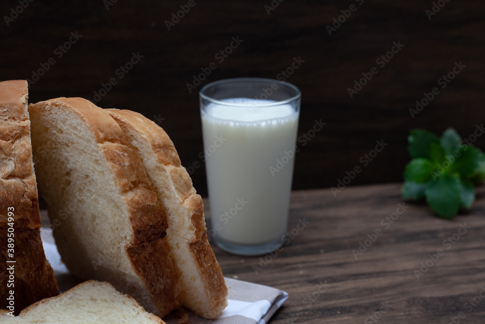Homemade bread in focus ahead with glass of milk and slightly blurred green leaves in the background. Wood background. Homemade bread in focus ahead with glass of milk and slightly blurred green leaves in the background. Wood background.