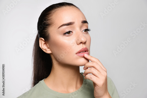 Woman with herpes touching lips on light grey background photo