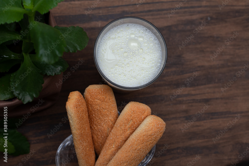 Brazilian champagne biscuit with glass of milk and vase with green leaves on top of wood. Top view with clean space for design. Brazilian champagne biscuit with glass of milk and vase with green leaves on top of wood. Top view with clean space for design.