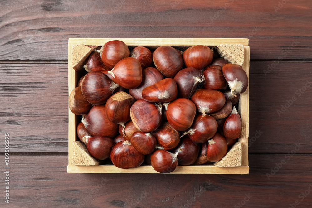 Obraz premium Fresh sweet edible chestnuts in crate on wooden table, top view