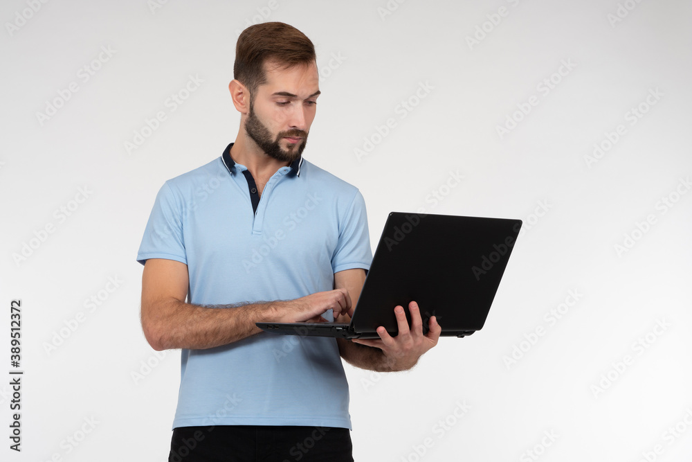 Man with a laptop in his hands. Portrait of man standing on a light background. Concept guy works as programmer. Guy uses a laptop while standing. He will program in computer. Portrait of programmer Man with a laptop in his hands. Portrait of man standing on a light background. Concept guy works as programmer. Guy uses a laptop while standing. He will program in computer. Portrait of programmer